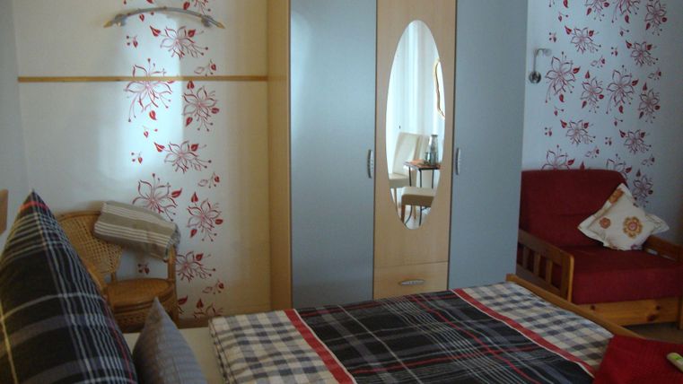 Ein gemütliches Schlafzimmer mit einem Doppelbett und einer roten Couch. An der Wand sind dekorative Blumenmuster und ein Kleiderschrank mit Spiegel.
