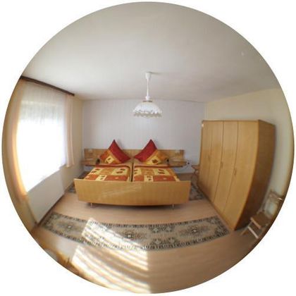 Ein gemütliches Schlafzimmer mit einem Doppelbett und roten Kissen. Der Raum ist hell mit einem großen Fenster und einem Holzschrank.