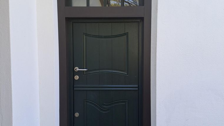 Eine grüne Haustür mit einem Fenster darüber. Der Eingang ist von einer weißen Wand umgeben und trägt die Inschrift "HAUS BVRG" sowie eine Jahreszahl.
