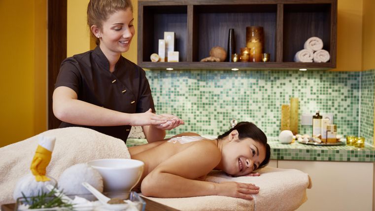 Eine entspannende Spa-Szene mit einer massierenden Therapeutin und einer zufriedenen Klientin. Im Hintergrund sind sanfte Farben und Wellness-Accessoires zu sehen.
