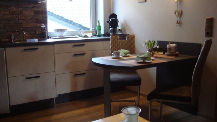 Eine moderne Küche mit einem runden Tisch und Stühlen. Auf dem Tisch stehen einige Gegenstände und das Licht ist warm und einladend.