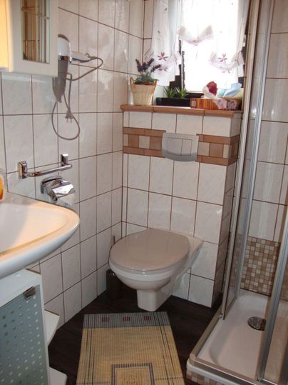 Ein kleines Badezimmer mit einer Toilette und einer Dusche. Es ist hell und modern mit weißen Fliesen und einer kleinen Fensterbank.