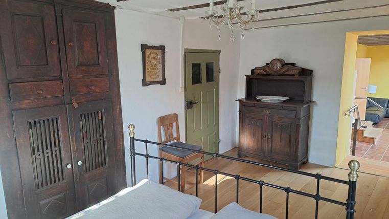 Ein gemütliches Schlafzimmer mit einem eleganten Bett und einem Holzschrank. Die Wände sind hell und die Decke hat dekorative Holzbalken.