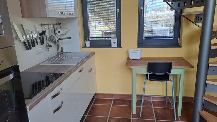 Eine moderne Küche mit einer Spüle, Herd und Küchenutensilien. Auf der gegenüberliegenden Seite steht ein kleiner Tisch mit einem Stuhl.