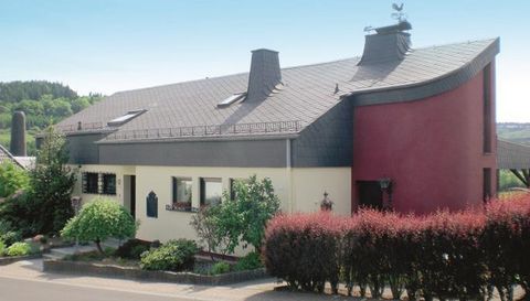 Ein modernes Haus mit einer auffälligen Architektur und einem gewellten Dach. Der Garten ist grün und gepflegt, umgeben von bunten Sträuchern.