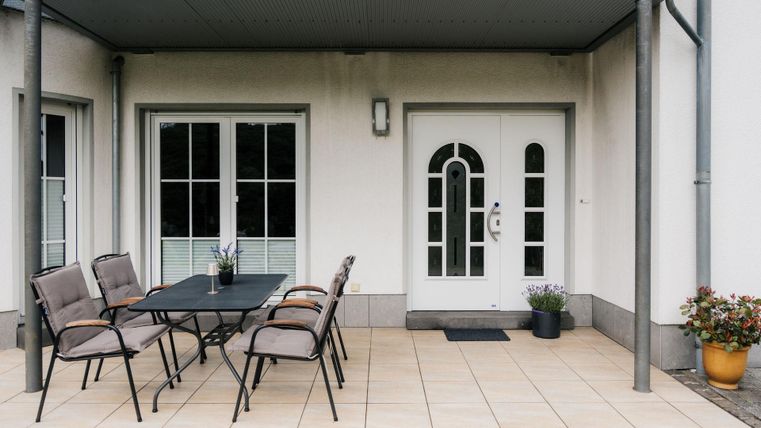Ein gemütlicher Außenbereich mit einem Tisch und Stühlen. Die Terrasse hat einen Eingangstür und einige Pflanzen.
