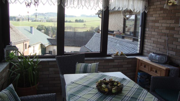 Ein gemütlicher Wintergarten mit einem Esstisch und Stühlen. Die großen Fenster bieten einen Blick auf die umliegende Landschaft.