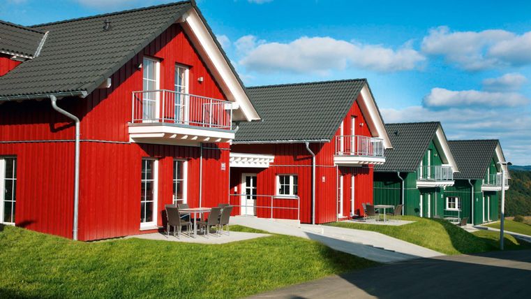 Bunte Ferienhäuser in angenehmer Umgebung. Die roten und grünen Häuser stehen auf einer grünen Wiese unter einem blauen Himmel.