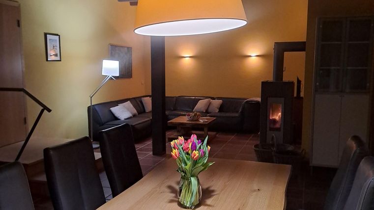 Ein gemütlicher Essbereich mit einem großen Holztisch und schwarzen Stühlen. In der Mitte steht eine Vase mit bunten Blumen und eine große Lampe hängt von der Decke.