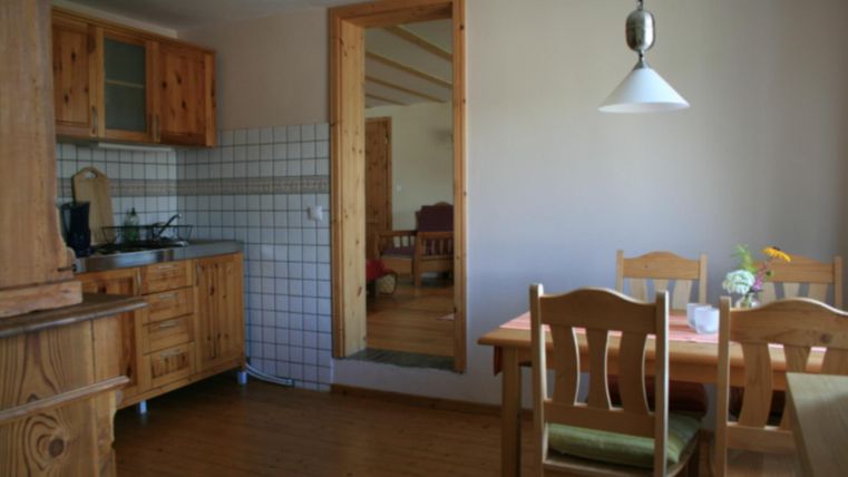 Eine gemütliche Küche mit Holzschränken und einem Esstisch. Durch einen Türdurchgang ist ein Wohnzimmer sichtbar.