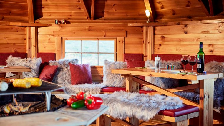 Ein gemütlicher Holzraum mit rustikalen Möbeln und weichen Felldecken. Auf dem Tisch stehen Snacks und Wein, perfekt für eine entspannte Zeit.