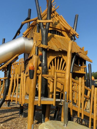Ein kindgerechter Spielplatz mit einer Holzstruktur in Form eines Hauses. Rutschbahnen und zahlreiche Klettermöglichkeiten laden zum Spielen ein.