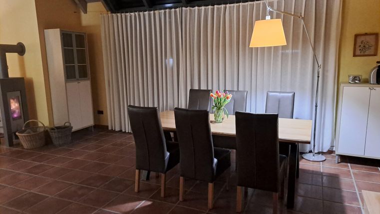 Ein moderner Essbereich mit einem großen Tisch und sechs Stühlen. Eine Stehlampe und ein Fenster mit Vorhängen sorgen für eine gemütliche Atmosphäre.