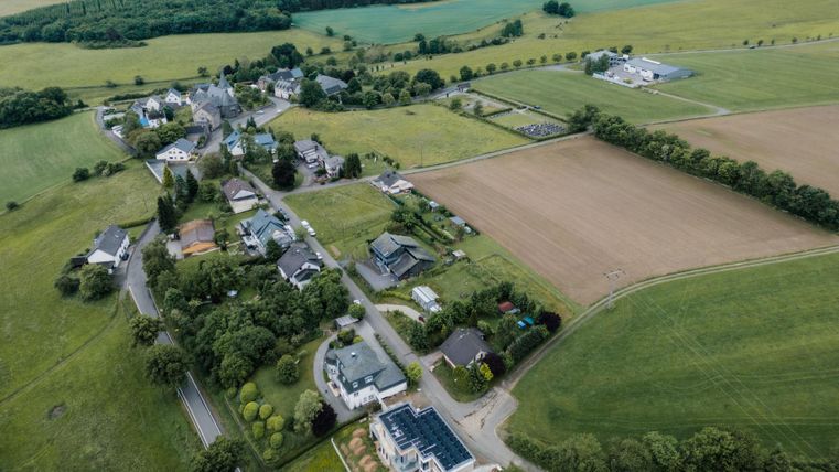 Eine ruhige ländliche Gegend mit einem kleinen Dorf und weiten Feldern. Die Landschaft ist grün und bewaldet mit verstreuten Häusern.