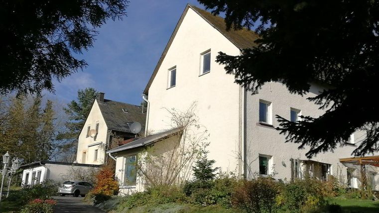 Ein modernes, helles Wohnhaus mit einem gepflegten Garten. Im Hintergrund sind Bäume und ein klarer Himmel zu sehen.