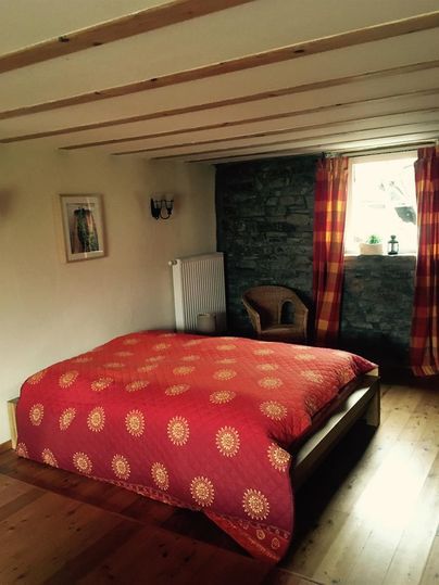 Ein gemütliches Schlafzimmer mit einem großen Bett und bunten Vorhängen. Die Wände sind teilweise mit Stein und Holz verkleidet, was eine warme Atmosphäre schafft.