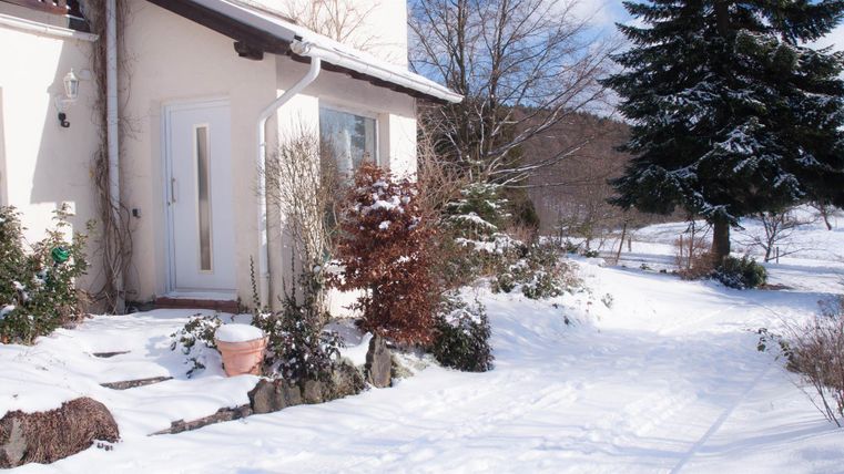 Ein hübsches Haus im Winter, umgeben von frischem Schnee. Die Landschaft ist ruhig und friedlich mit schneebedeckten Bäumen.