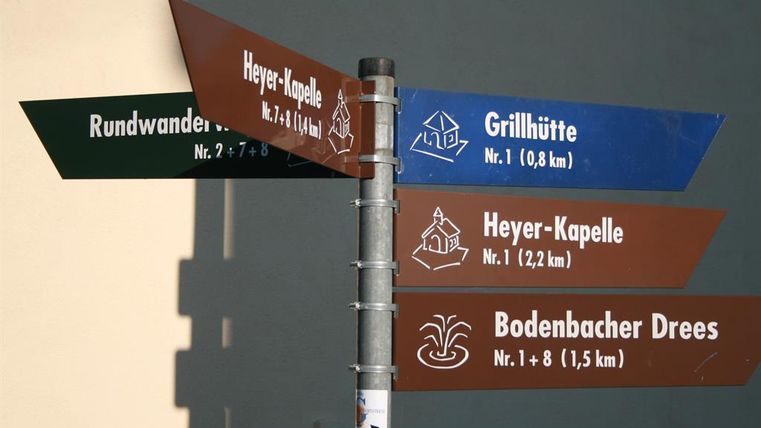 Ein Wegweiser mit unterschiedlichen Richtungen für Wanderungen. Es zeigt Entfernungen zu Grillhütte, Heyer-Kapelle und Bodenbacher Drees.